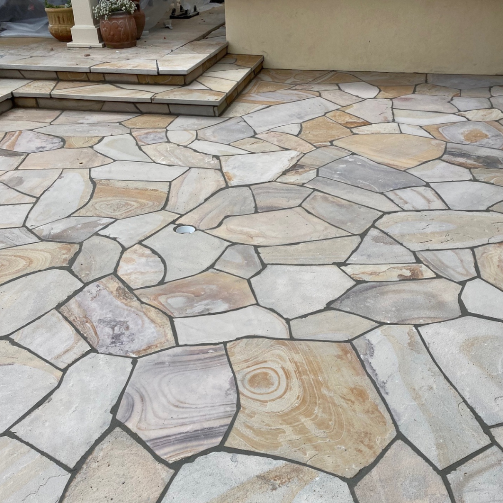 An image showcasing a breathtaking flagstone patio, highlighting the meticulous patio construction and expert flagstone patio installation. The natural stone laid out in an intricate pattern enhances the aesthetic beauty of the outdoor space, creating a seamless blend with the surrounding landscape.
