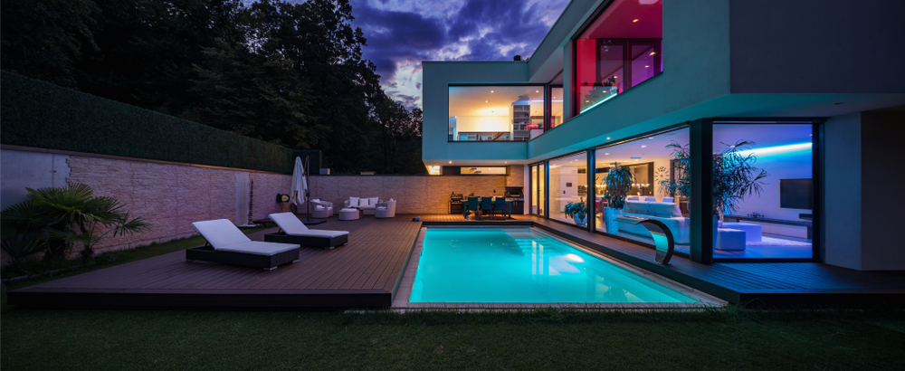 Image showcasing a modern backyard patio and pool in the evening with ambient lighting.